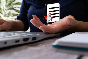 Woman working on laptop holding a document icon with rocket