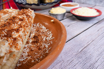 Corn on the cob prepared with cheese and spicy chili powder on a kitchen table, Mexican food