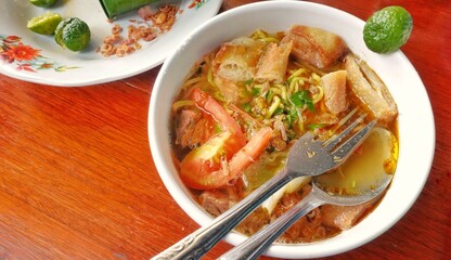 A typical Indonesian soup called Soto Mie Bogor is served in a bowl at the side of the table.