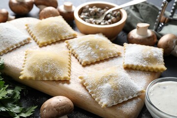 Uncooked ravioli and mushrooms on black table, closeup