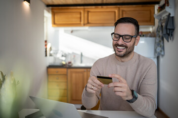 Happy man making online payment using credit card and laptop at home