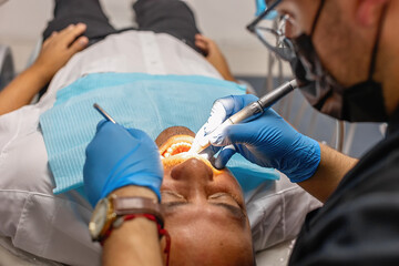 Male dentist working on a patient in a modern dental office. The patient lies relaxed in the chair...