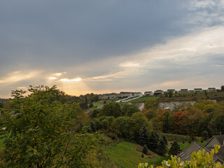 Fall sunlight breaks through the clouds, casting warm rays over an American neighborhood, bathing the scene in a golden glow.