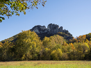 Summit of Seneca Rocks, West Virginia, framed by trees in fall colors, a meadow and a blue sky