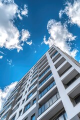 Modern apartment building reaching towards a vibrant blue sky, dotted with puffy white clouds.  A low-angle view emphasizes the building's height and architectural design