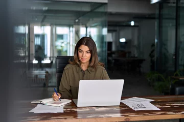 Gordijnen Busy 40 years old business woman employee or entrepreneur working in office taking notes in office. Businesswoman of middle age account manager executive using laptop computer at work. © insta_photos