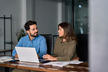 Fototapeta na wymiar Candid photo of two busy happy professional business people working in office with laptop computer. Middle aged female executive manager talking to male colleague having conversation sitting at work.