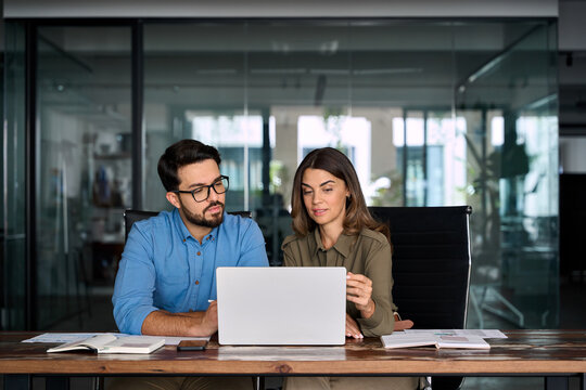 Mature executive manager talking to colleague explaining online project results having discussion at meeting. Two busy business people entrepreneurs team checking data using laptop at work in office.