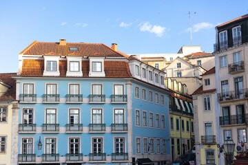 A charming blue building with traditional Portuguese architecture stands in a sunny street of Lisbon, Portugal, surrounded by colorful neighboring buildings and ornate wrought-iron balconies.