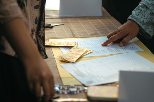 One person, partially visible on the left, appears to be standing next to the table, while another person on the right is pointing with their finger at a document laid out on the table