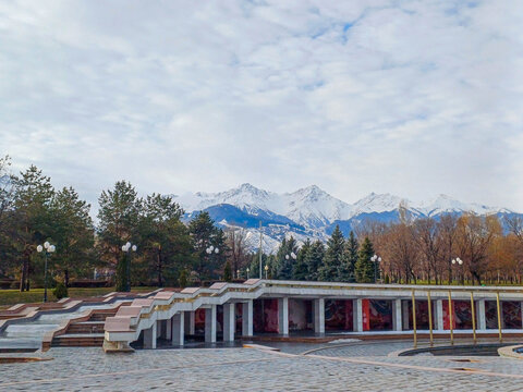 Amfiteater Rača, featuring its stepped architectural design and open-air structure, located within President's Park. The amphitheater is set against a backdrop of snow-capped mountains under a cloud