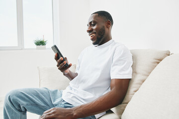 Smiling African American man using smartphone while sitting comfortably on a couch, showcasing modern lifestyle and relaxation at home