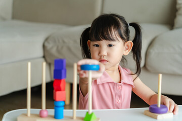 3 year old girl having fun playing with colorful geometric shape wooden blocks educational toys at...