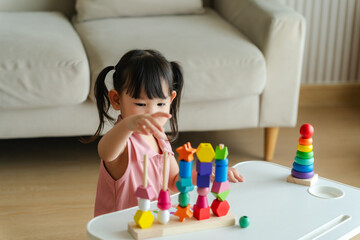 3 year old girl having fun playing with colorful geometric shape wooden blocks educational toys at...