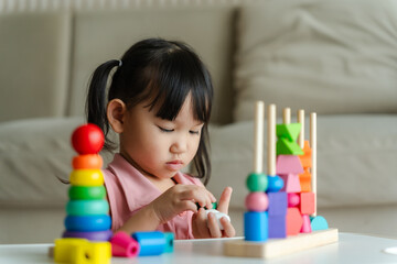 3 year old girl having fun playing with colorful geometric shape wooden blocks educational toys at...