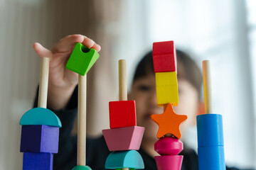 Close-up of 3 year old girl's hands having fun playing with colorful geometric shape wooden blocks educational toy at home. Selective focus. Childhood and children learning concept.