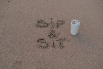 Sip and Sit – Handwritten Message on Volcanic Sand with Thermos Mug
