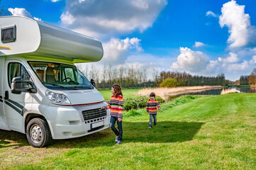 Kids near camper (rv) playing and have fun, family travel in motorhome on holiday vacation trip in camping