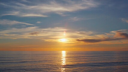 Obraz premium The sky is blue and the sun is setting. The water is calm and the horizon is visible