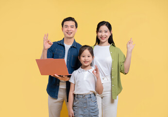 Happy family of three including a child posing in front of a yellow backdrop with a laptop