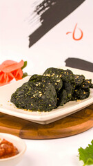 A beautifully arranged plate of dark green snacks garnished with sesame seeds, alongside sauces and decorative elements