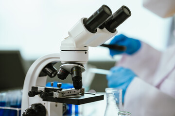 A scientist conducts chemical research in a laboratory using a microscope and pipette, analyzing liquids for medical and biotechnology development.