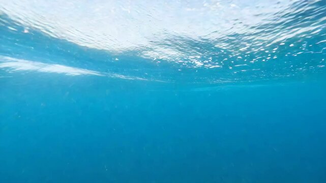 Cinematic underwater view with clear blue water and light reflections on the surface