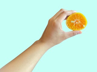 A hand holding a fresh and juicy orange, perfect for summer designs. There is a plain background...