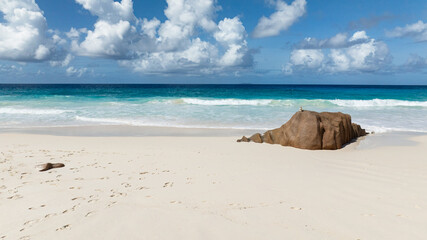 Rocky outcrop on a clear sandy beach with turquoise sea. La Digue, Seychelles. Petite Anse Beach.