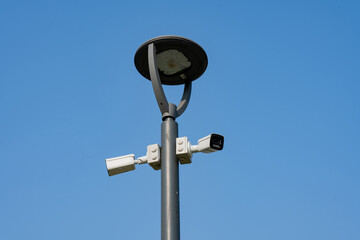 Two Security CCTV camera on gray steel post and solar garden lamp or light with clear blue sky, copy space, urban urban park surveillance cameras, Jakarta Garden