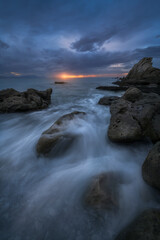 Long exposure of ocean waves flowing over rocks at Azkorri beach, Getxo, Spain, during sunset with dramatic storm clouds