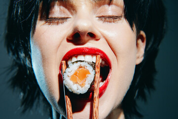 A young woman with short black hair passionately eating sushi using chopsticks, showcasing...