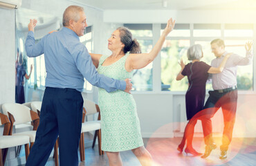 Happy mature woman enjoying impassioned merengue with male partner in latin dance class. Social...