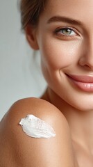 A young woman smiles, showing glowing skin with moisturizer applied to her shoulder, highlighting healthy skincare and natural beauty.