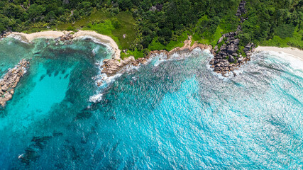 Top view of clear turquoise water meeting a rocky beach and lush green forest. Seychelles, La Digue.