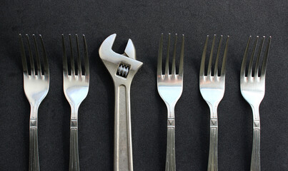 A metal adjustable spanner in a row of metal table forks. Conceptual photo on the topic of originality and personalization
