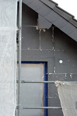 A wall of a house covered with EPS graphite polystyrene boards for thermal insulation, a window covered with a protective film, a scaffolding