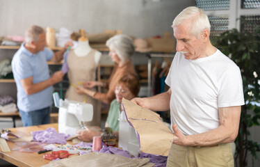 In training tailoring workshop for older adults, elderly man reviewing paper pattern pinned to...