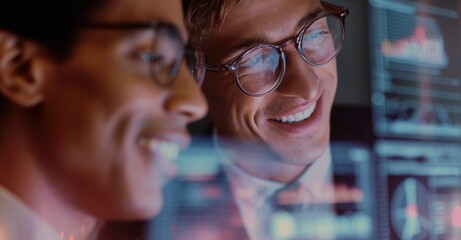 Two colleagues, wearing glasses, analyze data on a screen with charts and graphs. They appear to be working together with positive attitudes.