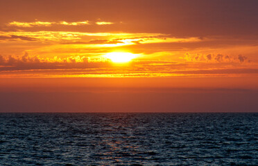 Fototapeta premium The sun is setting over the ocean, casting a warm glow on the water