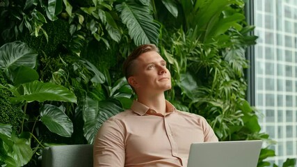 Man working on laptop in office near green plant wall feeling calm and hopeful indoors