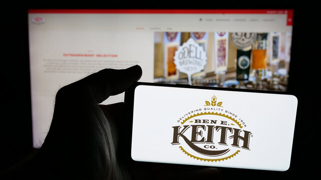 Stuttgart, Germany - 05-16-2025: Person holding mobile phone with logo of US distribution business Ben E. Keith Company on screen in front of web page. Focus on phone display.