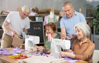 Elderly participants in educational coterie study sewing. Some people communicate and discuss pattern, while others sew using sewing machine..