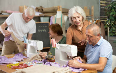 Elderly woman teacher shows group of elderly men and women how to sew on sewing machine in class
