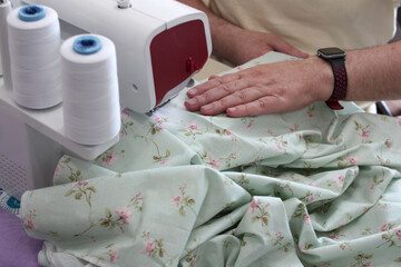 Hands of a tailor working with an overlocker. Overcasting fabric on an overlocker. Concept of sewing baby diapers, bed linen.