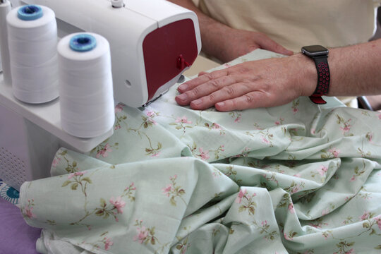 Hands of a tailor working with an overlocker. Overcasting fabric on an overlocker. Concept of sewing baby diapers, bed linen.