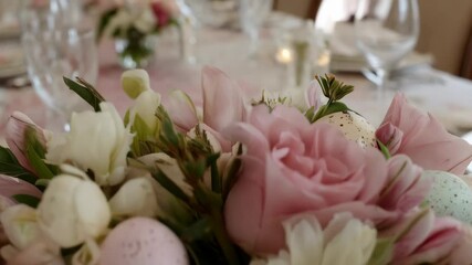 Elegant Easter centerpiece featuring pink roses, white flowers, and pastel colored decorative eggs on a formal dining table setting