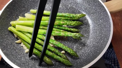 Fresh green asparagus spears sizzle in a non-stick pan, highlighting healthy cooking and spring cuisine - Powered by Adobe