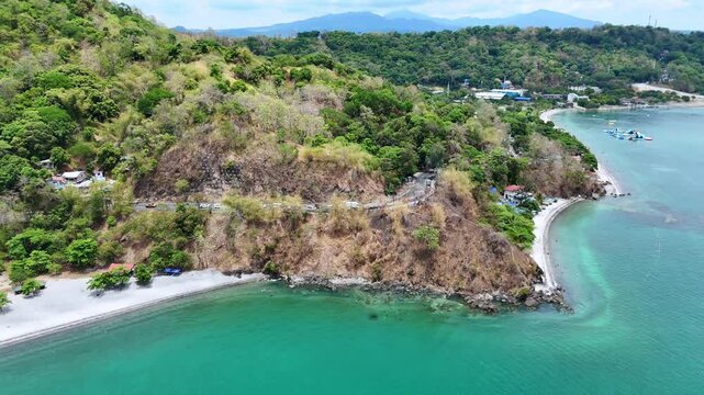 Aerial 4K morning drone footage of Mabayuan Beach in Olongapo, Zambales, Philippines, showing turquoise waves lapping white sand with rugged mountains and a distant city skyline.