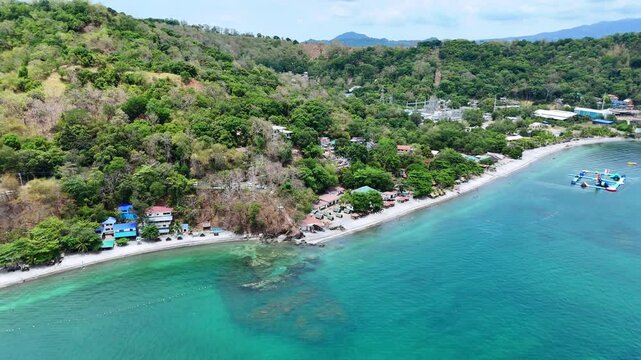 Aerial 4K morning drone footage of Mabayuan Beach in Olongapo, Zambales, Philippines, showing turquoise waves lapping white sand with rugged mountains and a distant city skyline.